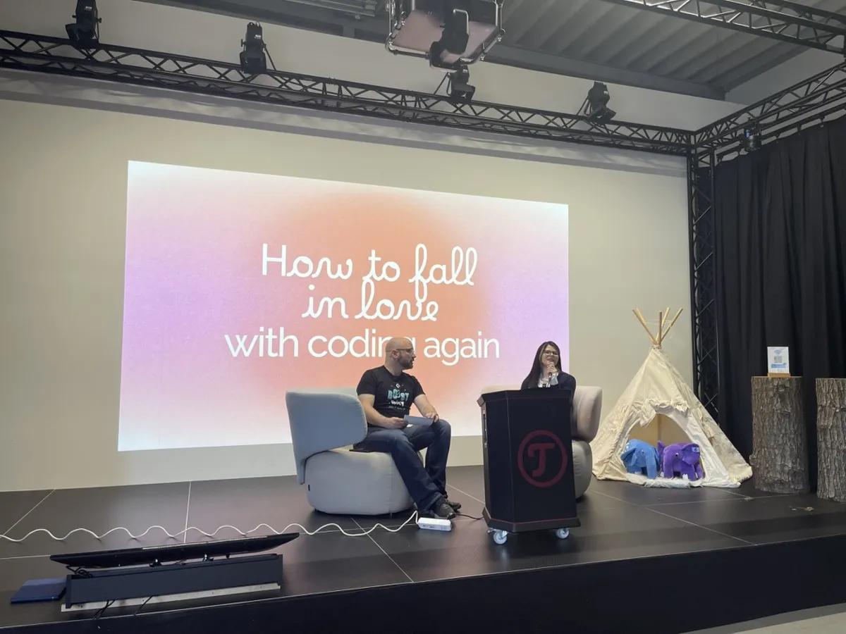 Zwei Personen in Sesseln auf der Bühne vor der Folie How to fall in love with coding again