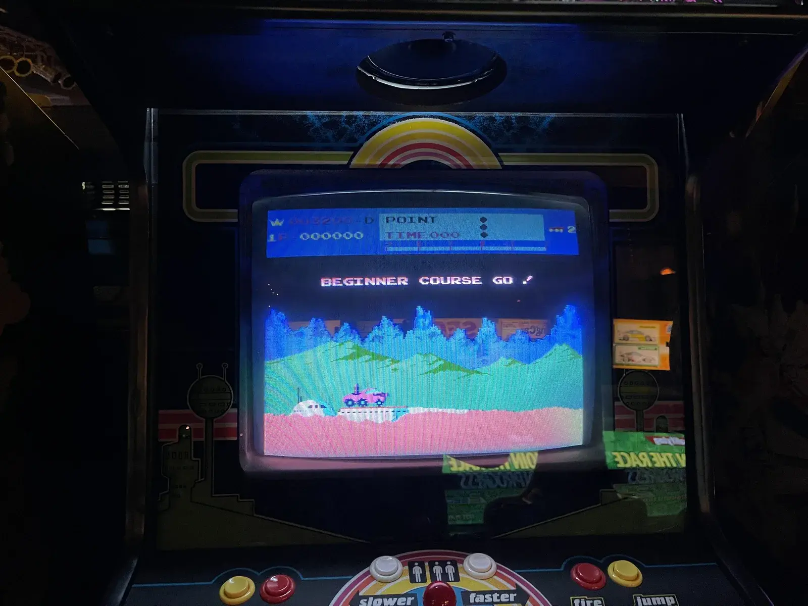 Der Automat Moon Patrol mit der Bildschirmmeldung Beginner Course Go, im Bild der Mondbuggy vor mehreren Gebirgsebenen, darunter Knöpfe für langsamer, schneller, Feuer und Sprung