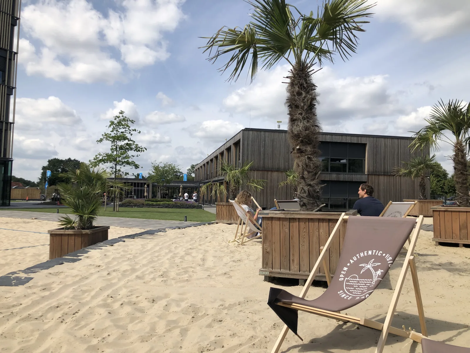 Angelegter Strandbereich vor dem Shopware-Gebäude mit Sand, Palmen und Liegestühlen, auf denen Open, Authentic, Visionary steht